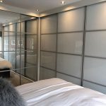 Made to measure crittall mirrored sliding doors combined with Crittall style grey glass sliding doors as part of a corner sliding door wardrobe installation