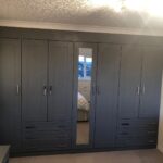 A wall to wall hinged wardrobe with external drawers.