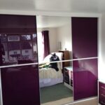 Minimalist three door sliding wardrobe with purple glass and a mirror fitted