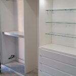 Sliding wardrobe interior fitted with glass shelving, lighting, drawers and hanging space.