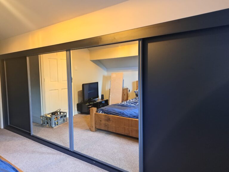 Harrison Monarch sliding door wardrobes in the colour Graphite. Two doors are fitted with Indigo Blue panels, two door are fitted with mirrors.