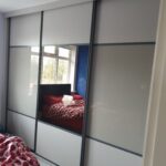 Harrison Monarch sliding door wardrobes fitted with Cashmere Oak panels, Stone Grey coloured glass and a mirror.