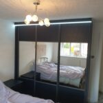 Fitted three door sliding wardrobe with Indigo Blue panels and mirrors fitted into each door. An LED light strip is fitted above the wardrobes.