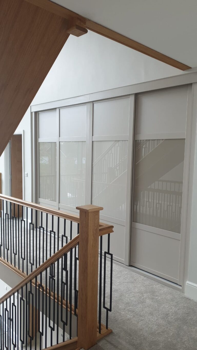 Fitted sliding door wardrobe with four doors. The two outer doors are fitted with Cashmere coloured panels and Stone Grey coloured glass. The two centre doors are fitted with Cashmere coloured panels and Cashmere coloured glass. The exterior and surround is also in the colour Cashmere.