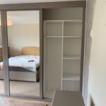 Fitted sliding door wardrobes with mirrored doors and light grey coloured frames - White interior with shelves