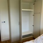 Interior of a bespoke fitted hinged door wardrobe. A top shelf, long hanging section and a bottom shelf for shoes are fitted. A tie rail is also fitted to the back of one door