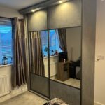 Bespoke fitted sliding door wardrobes fitted with lights above. Both doors are finished with graphite frames and split with a concrete coloured panel at the top and bottom and a large mirror in the centre