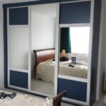 Fitted sliding door wardrobes with light grey frames, blue panels and mirrors.