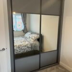 Bespoke fitted sliding door wardrobes in the colour Graphite. Both doors are split with Graphite panels at the top and bottom and a large mirror in the centre