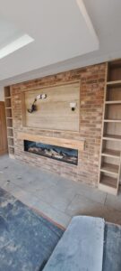 Media wall build with red bricks. An integrated fire is fitted with a Halifac Oak matelpiece,. A recess is included with a Halifax Oak back board and trim for the TV to fit into. Halifax Oak shelving is fitted either side of the brickwork, floor to ceiling.