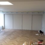 Bespoke fitted sliding door wardrobes fitted into a room with a low ceiling. The doors are light grey in colour.