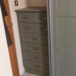 Bespoke fitted drawer unit between a wall and a siding door wardrobe. The unit is six drawers high, with the top two drawers split into two. The drawers are in the shaker style, Reed Green Oak colour finish