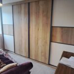 Bespoke fitted sliding door wardrobes, four doors. The two centre doors are fitted with wood effect panels. The two centre doors are fitted with cream panels and a small piece of wood effect in the centre.