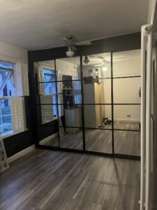 Bespoke fitted sliding door wardrobes in the colour black. There are four doors, each door is in the crittal style.