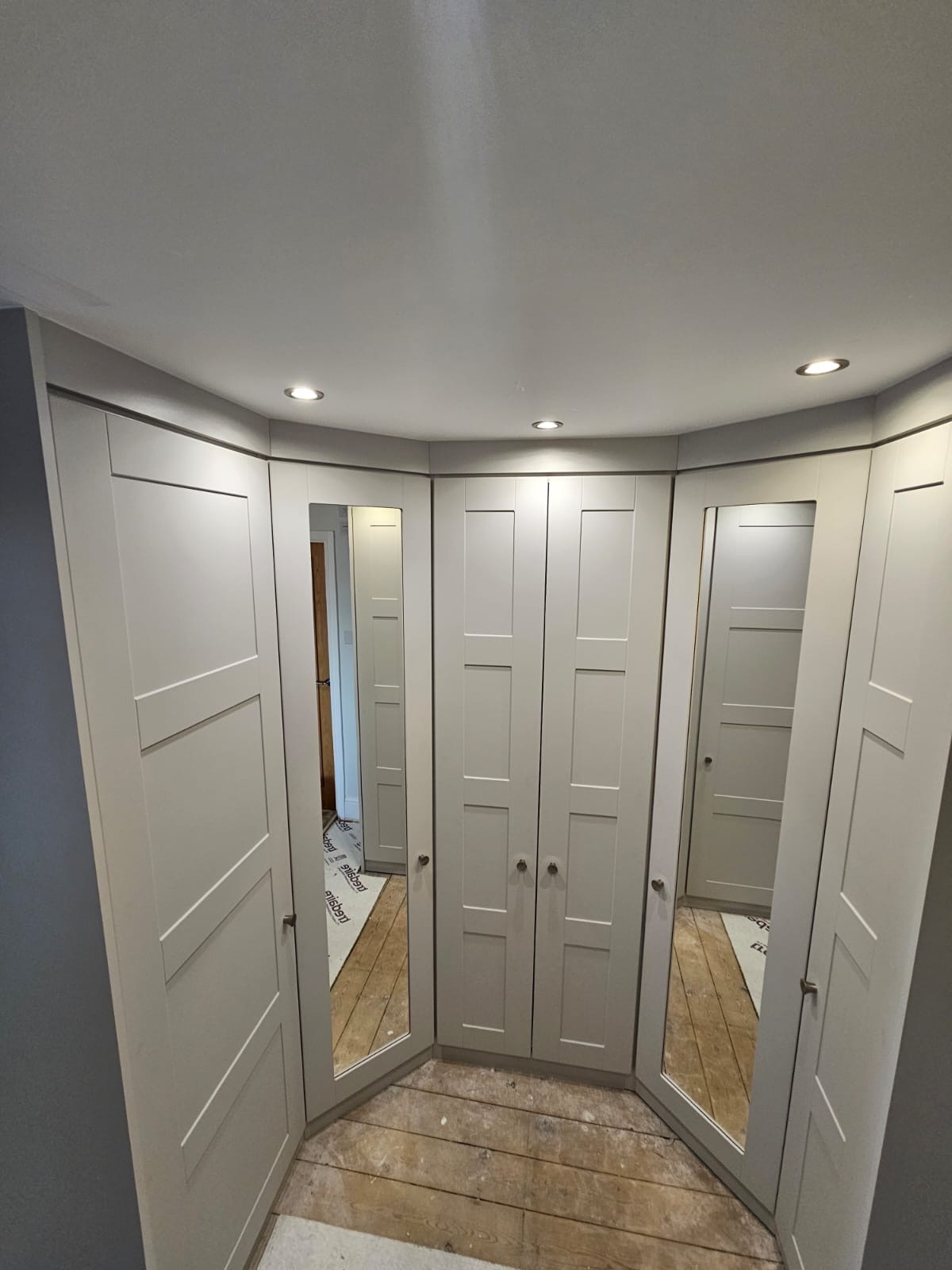 'U' shaped fitted wardrobes in the Shaker style. There is a double wardrobe in the centre, single mirrored corner wardrobes either side and single solid wardrobes either end.