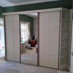 Bespoke Shaker sliding door wardrobe with two cream panelled wardrobe doors and one mirrored wardrobe door.