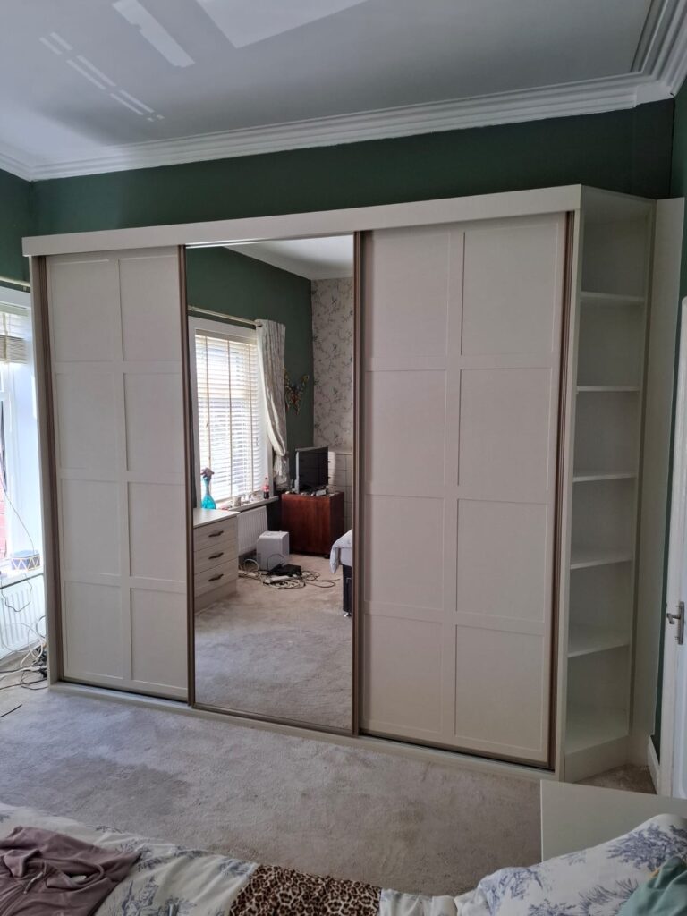 Bespoke Shaker sliding door wardrobe with two cream panelled wardrobe doors and one mirrored wardrobe door.