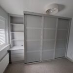 Fitted bedroom furniture consisting of a custom wardrobe with panelled sliding doors and bespoke drawers and shelving.