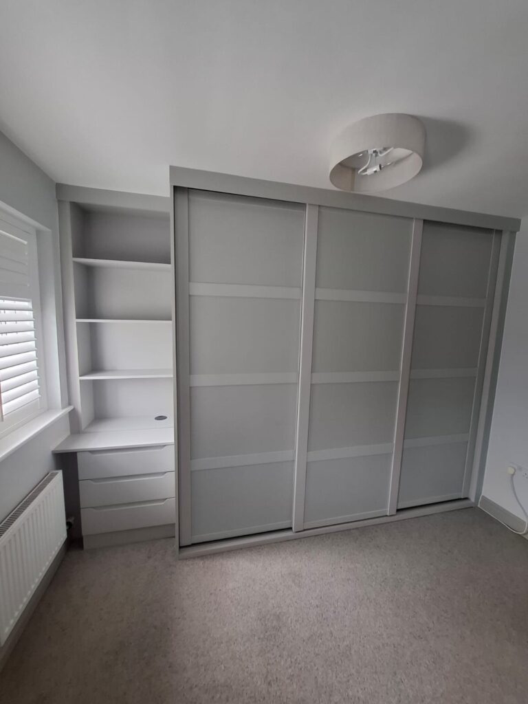 Fitted bedroom furniture consisting of a custom wardrobe with panelled sliding doors and bespoke drawers and shelving.
