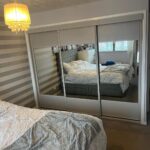 Grey 3 door sliding wardrobe with mirror built into a wall