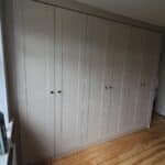 three double wardrobes fitted to a wall on the left. The wardrobe doors are in the shaker style and in the colour Cashmere Grained.