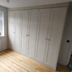 three double wardrobes fitted to a wall on the left. The wardrobe doors are in the shaker style and in the colour Cashmere Grained.
