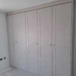 Two double wardrobes and one single wardrobe fitted to a wall on the left. The wardrobe doors are in the shaker style and in the colour Cashmere Grained.