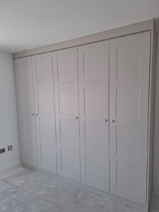 Two double wardrobes and one single wardrobe fitted to a wall on the left. The wardrobe doors are in the shaker style and in the colour Cashmere Grained.