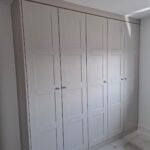 Two double wardrobes and one single wardrobe fitted to a wall on the right. The wardrobe doors are in the shaker style and in the colour Cashmere Grained.