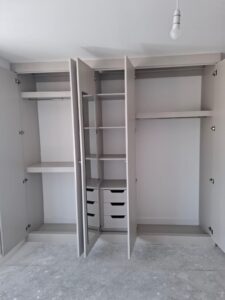 Fitted wardrobe interior with hanging space, shelving, drawers and a mirror.