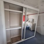 Fitted sliding door wardrobe with two mirrored sliding doors in the colour white. The inside can be seenw ith bespoke hanging rails fitted around a wall nib