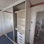 Fitted sliding door wardrobe with two mirrored sliding doors in the colour white. The inside can be seen with bespoke drawers, shelving and hanging rails.