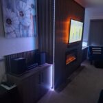 bespoke media wall with acoustic wall paneling and an intergrated electric fire. Custom living room cupboards are fitted either side of the media wall in a grey brown wood geain finish. fitted by Creative Joinery