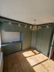 Fitted bedroom furniture with corner wardrobes and matching drawers in Reed Green finish with gold handles.