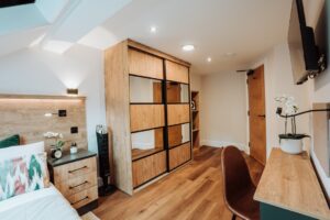 custom sliding door wardrobe with wood grain and mirrored doors. Accompanied by a matching custom bedside drawers in two tone wood grain and dark grey finish.