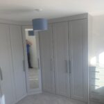 Custom corner wardrobe with Shaker style doors in a neutral light grey finish.