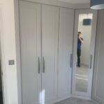 Custom corner wardrobe with Shaker style doors in a neutral light grey finish.
