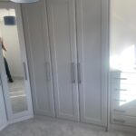 Custom wardrobes and tallboy drawers with Shaker style doors in a neutral light grey finish.
