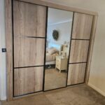 Bespoke wood effect sliding door wardrobes with black trim. One mirror door, two panel doors.