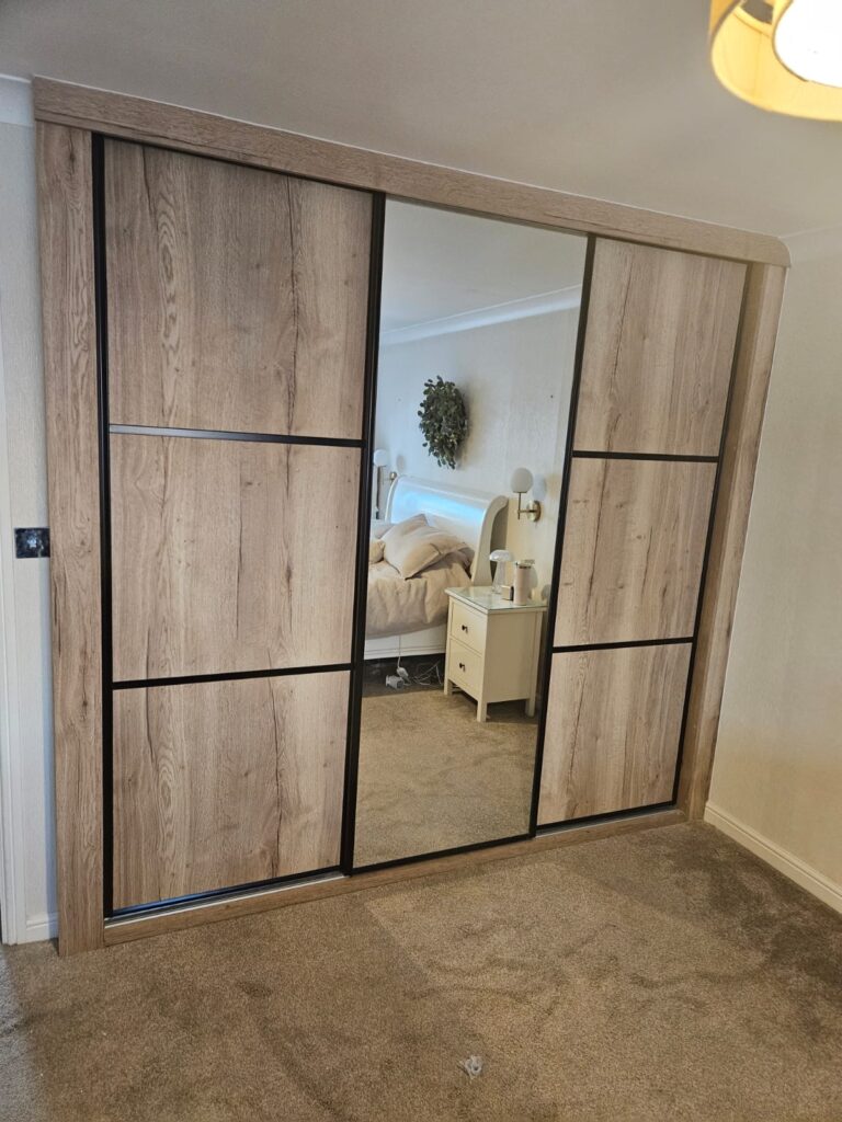 Bespoke wood effect sliding door wardrobes with black trim. One mirror door, two panel doors.