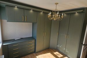 Fitted bedroom furniture with corner wardrobes and matching drawers in Reed Green finish with gold handles.
