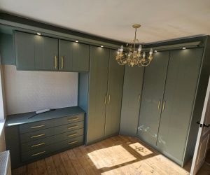 Fitted bedroom furniture with corner wardrobes and matching drawers in Reed Green finish with gold handles.