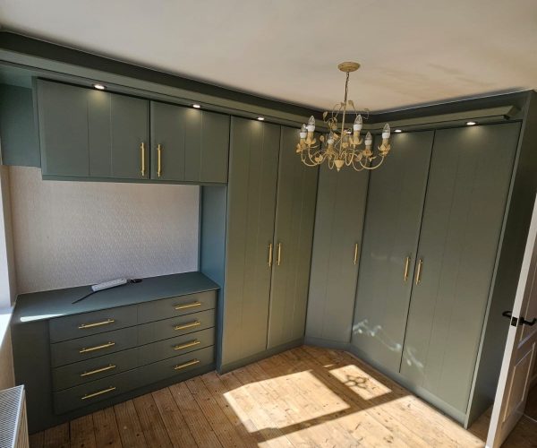 Fitted bedroom furniture with corner wardrobes and matching drawers in Reed Green finish with gold handles.