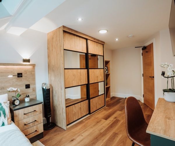 custom sliding door wardrobe with wood grain and mirrored doors. Accompanied by a matching custom bedside drawers in two tone wood grain and dark grey finish.