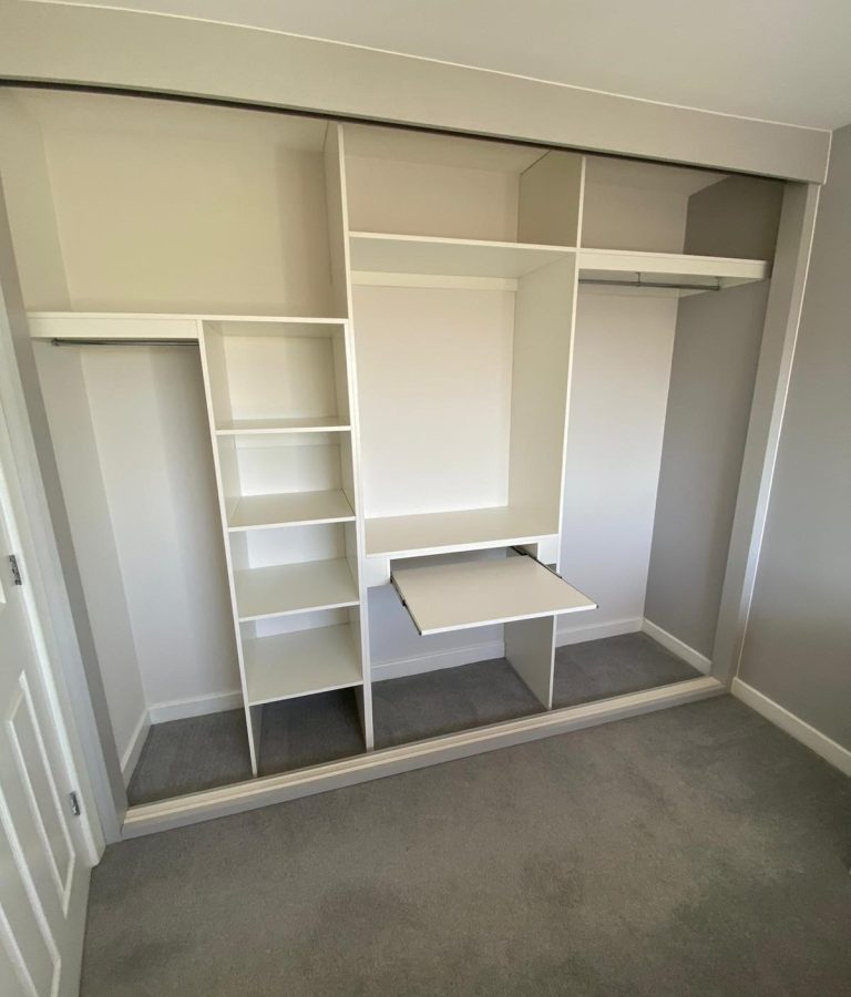 Integrated pull-out desk within a wardrobe interior for compact workspace use.